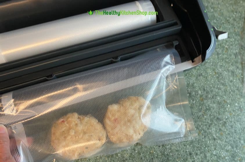 Two crab cakes placed in bag ready to be vacuum sealed. Top, open edge of bag is placed in the drip tray.